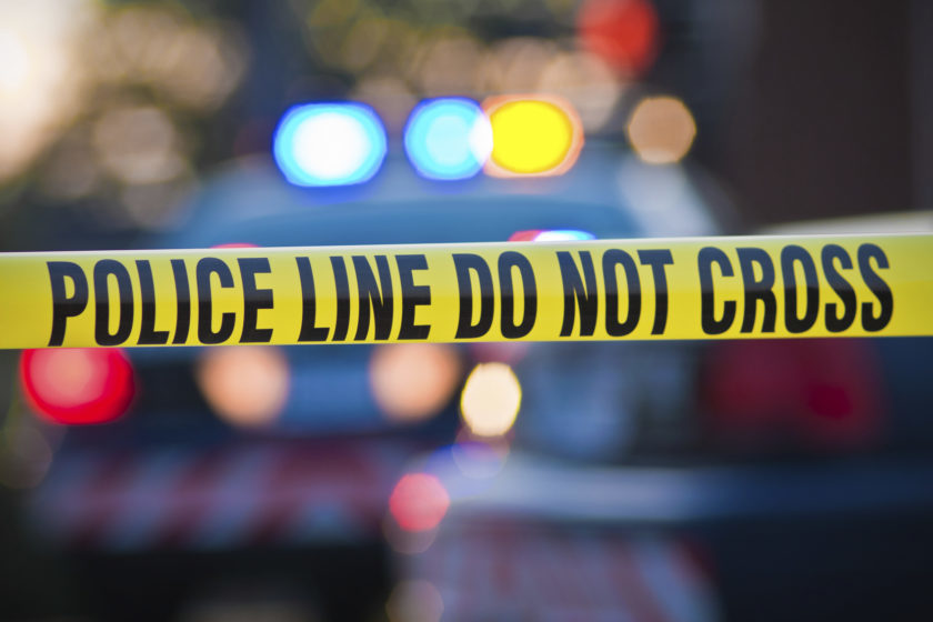 Shallow depth of field image taken of yellow law enforcement line with police car and lights in the background.