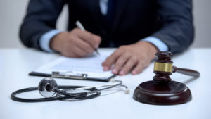 Lawyer signing workers' compensation claim, banging gavel near stethoscope