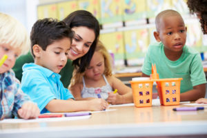 Group Of Elementary Age Children In Art Class With Teacher Using Crayons Drawing