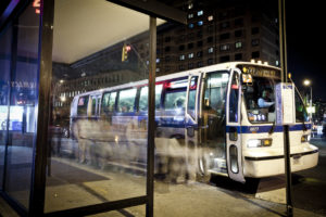 People are lining up at the bus stop and getting on the bus.