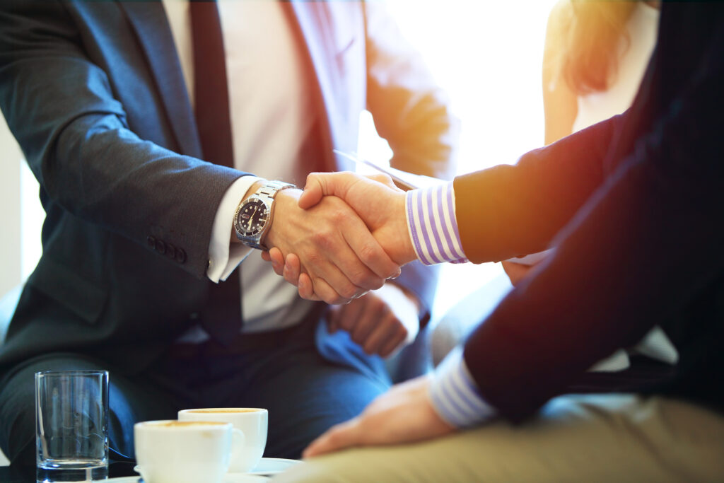 Business professionals shaking hands during a meeting, symbolizing a successful agreement, partnership, or legal settlement in a professional office setting. Business professionals shaking hands during a meeting, symbolizing a successful agreement, partnership, or legal settlement in a professional office setting.