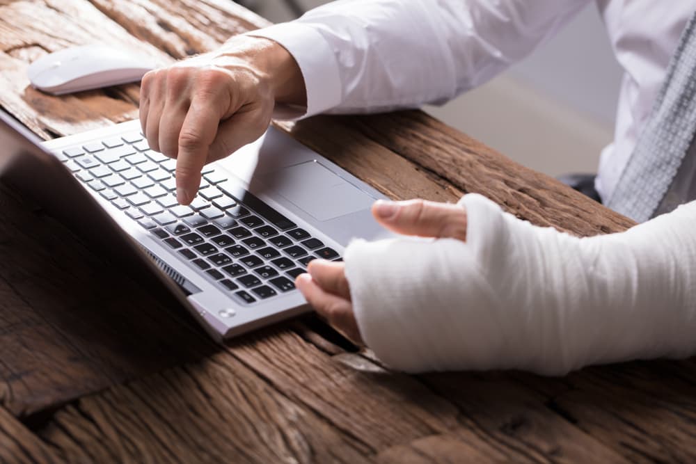 A close-up of a businessperson's hand with a hand injury, using a laptop.