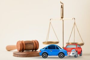 Two small toy cars, depicting a crash, sit on a courtroom table alongside a judge’s gavel. This setup symbolizes lawyer services, civil court trials, vehicle accident case analysis, and insurance coverage disputes.