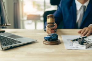 A lawyer, judge’s gavel, and a miniature car placed on a table symbolize court proceedings or auction actions involving a driver involved in an accident who received car insurance compensation.