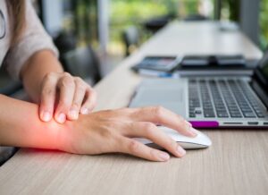Close-up of a woman holding her wrist, experiencing pain from prolonged computer use. Office syndrome causing hand discomfort due to repetitive strain.