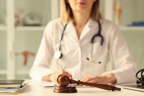 A female doctor sits at a desk with a gavel placed prominently in front, symbolising the intersection of healthcare and legal issues, possibly relating to medical malpractice or expert testimony.