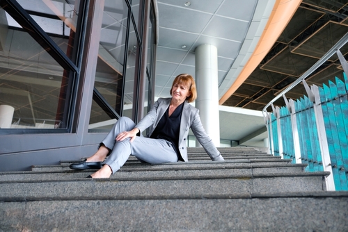 Injured woman in business attire sitting on outdoor steps, appearing to be in pain after a fall near a commercial building entrance.