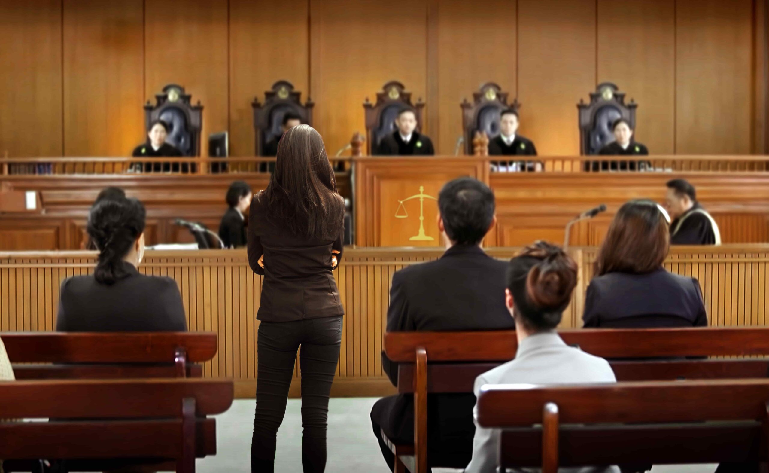 Attorney standing before judges in courtroom during trial, legal proceedings with seated audience