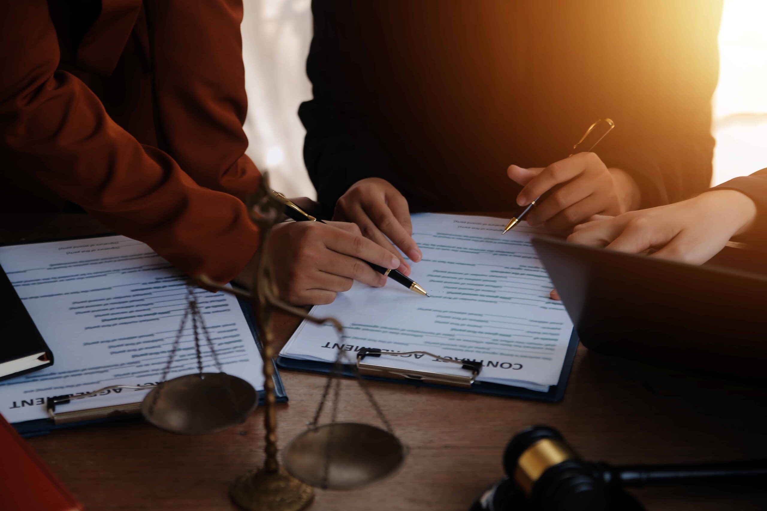 Legal professionals reviewing and signing a contract at a desk with scales of justice and a gavel, representing legal consultation, contract agreement, and workers’ compensation or personal injury law.