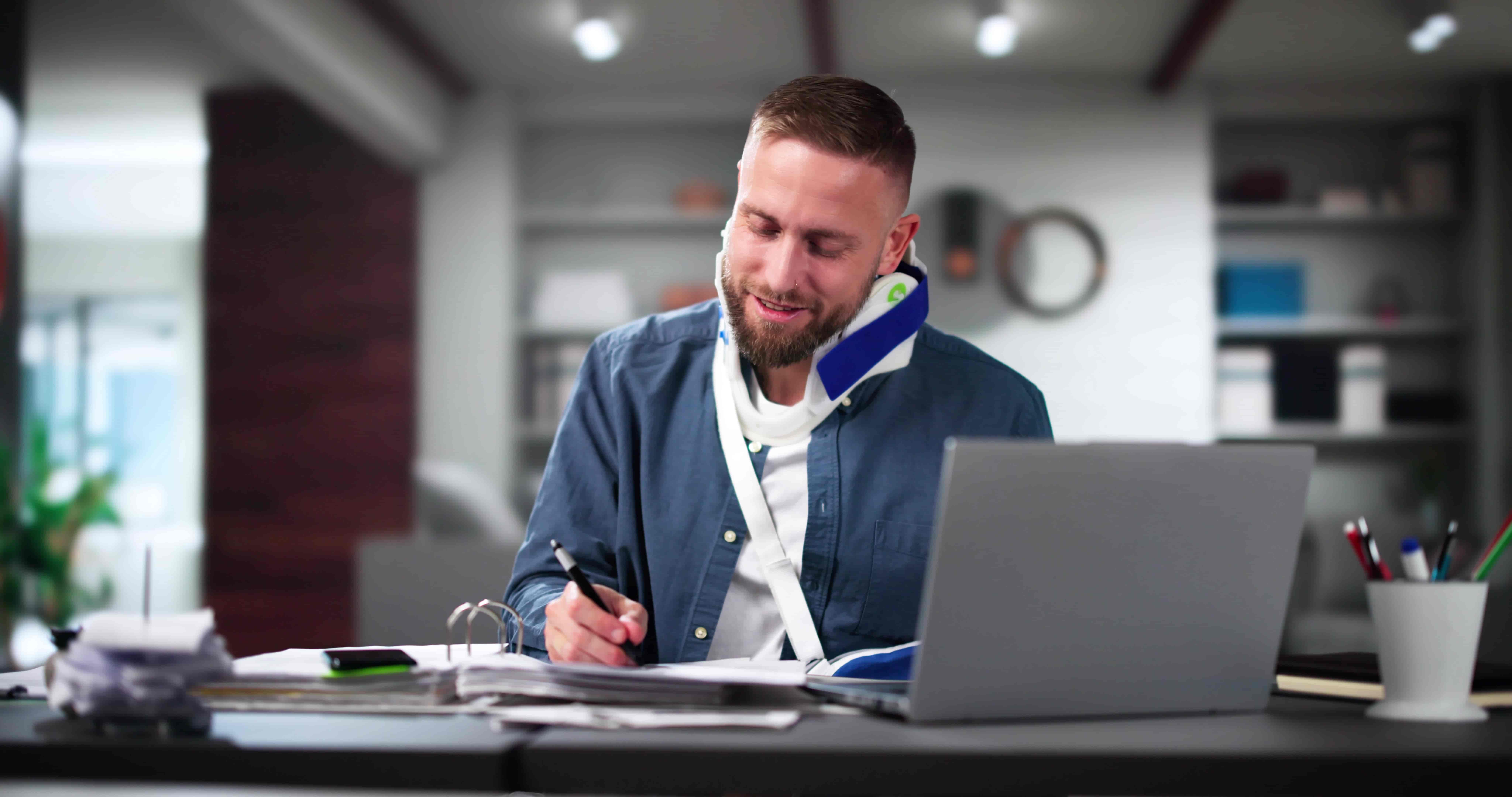 Injured office worker wearing a neck brace completing paperwork at a desk with a laptop, representing workplace injury recovery, workers’ compensation claim, and return-to-work process.