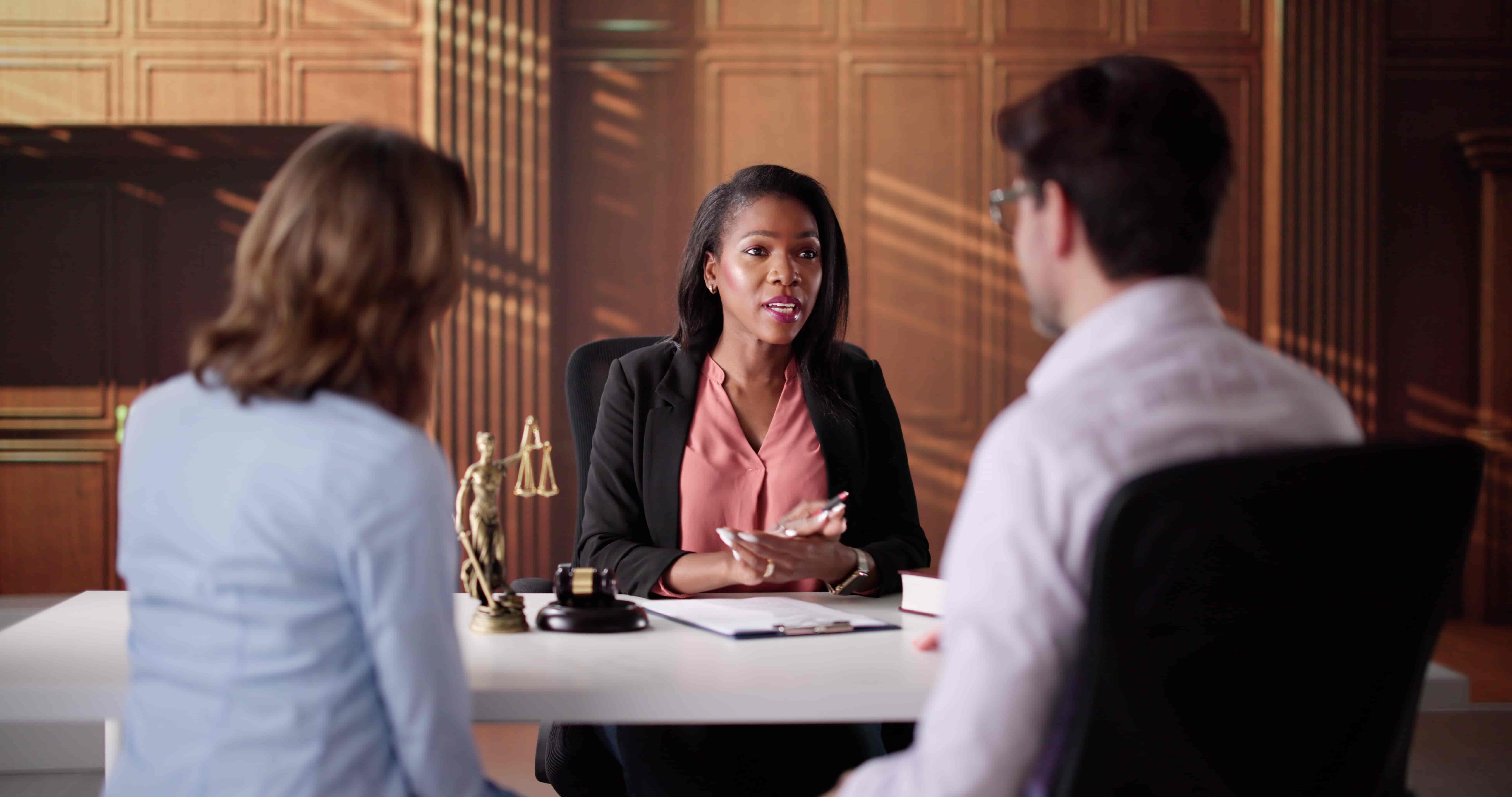 Workers’ compensation attorney meeting with clients in a law office, discussing a legal case at a desk with scales of justice, representing workplace injury consultation and legal advice.