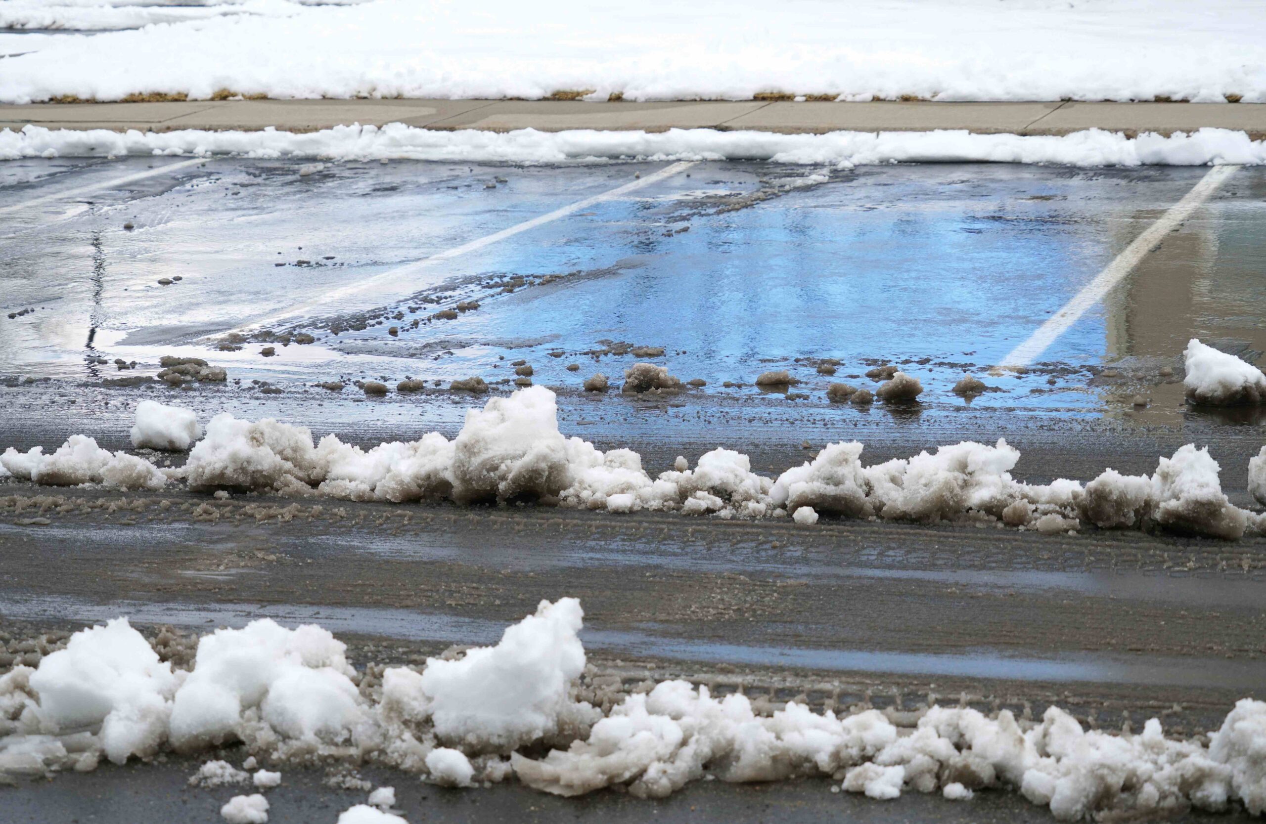 Parking lot with cleared lanes but untreated pedestrian walkway in winter